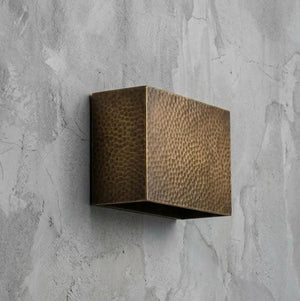 A square wall-mounted light fixture with a hammered metallic bronze finish, mounted on a textured gray concrete wall.