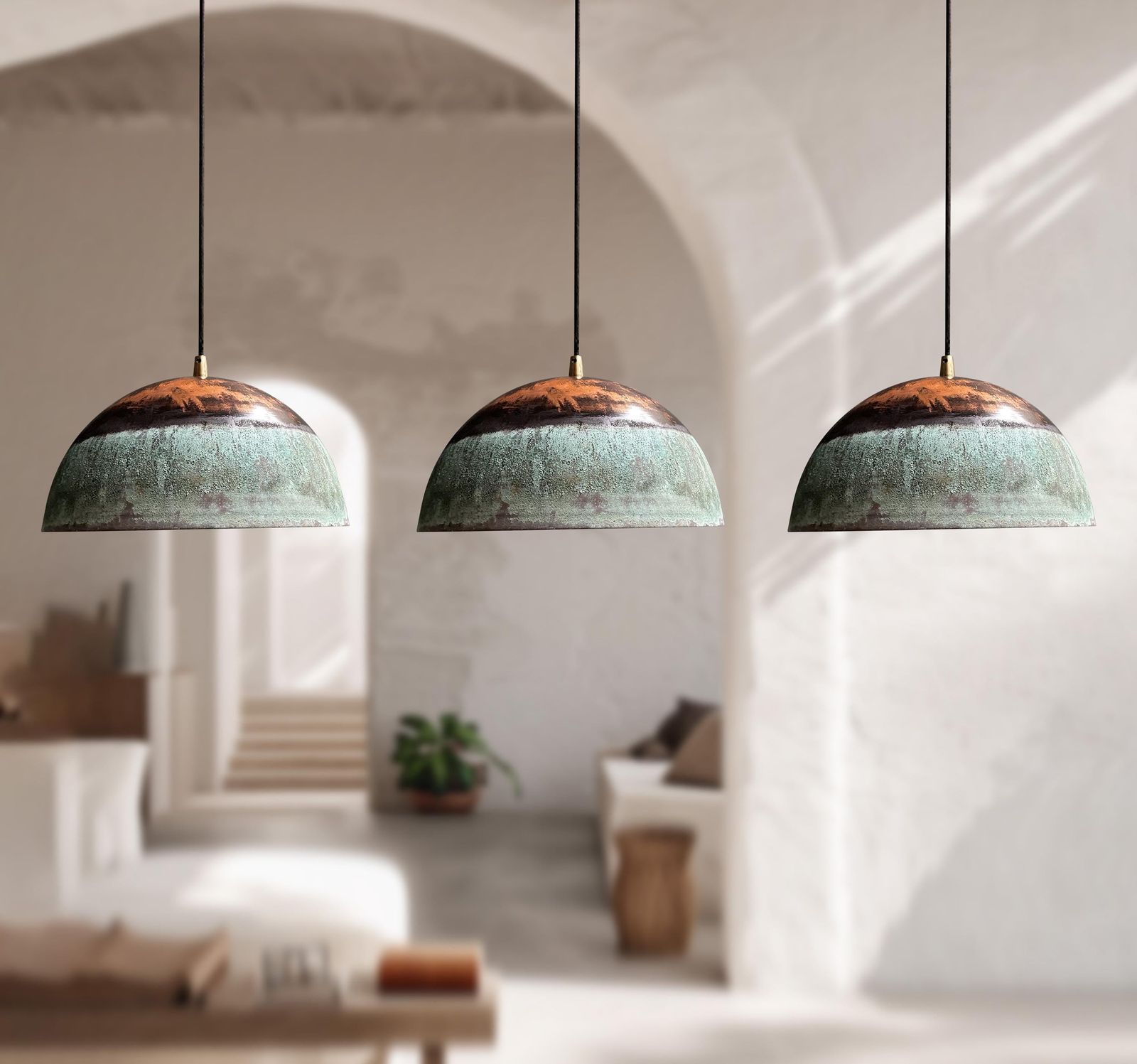 Three pendant lights with green and copper design hanging in a room with white walls and a window.