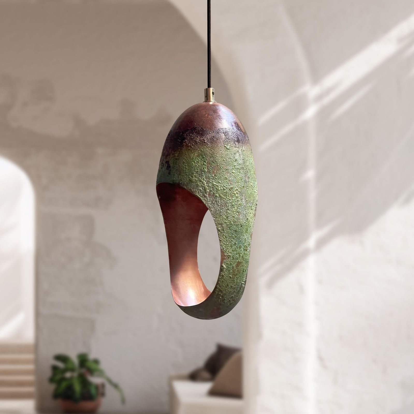 Uniquely shaped green pendant light hanging in a room with a plant and sofa.
