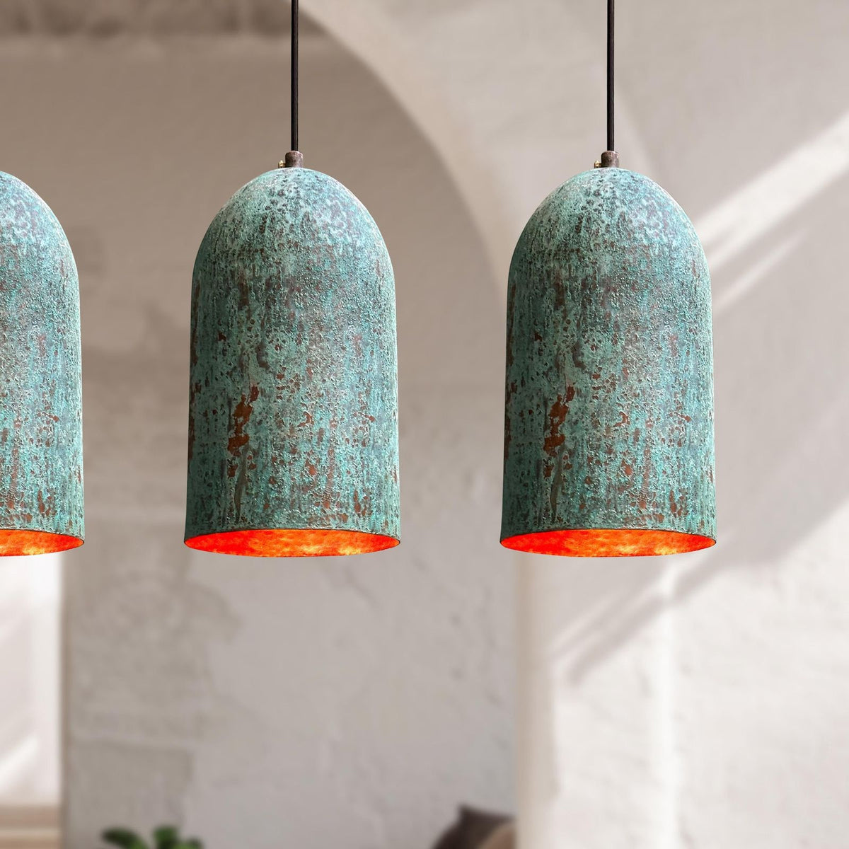Three rustic pendant lights with turquoise shades and orange interiors hanging against a neutral background.