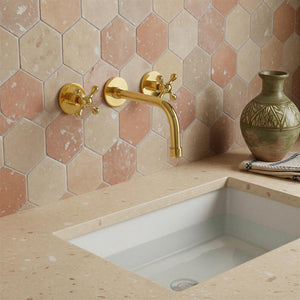 Bathroom sink with gold faucet against a hexagonal tile wall.