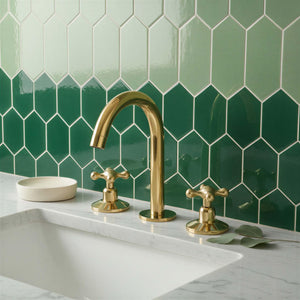 Gold faucet and handles on a kitchen sink with green tiled wall