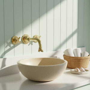 Bathroom setup with a beige sink, gold faucet, and a basket of towels against a light green paneled wall.
