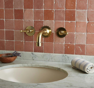 Bathroom sink with gold fixtures against a tiled wall.