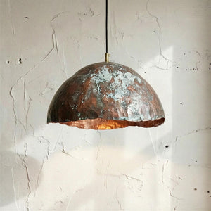 Copper pendant light hanging against a textured white wall