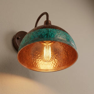 A wall-mounted sconce with a hammered copper-toned dome shade and a turquoise-green textured band around the upper rim, shown lit against a plain beige wall.
