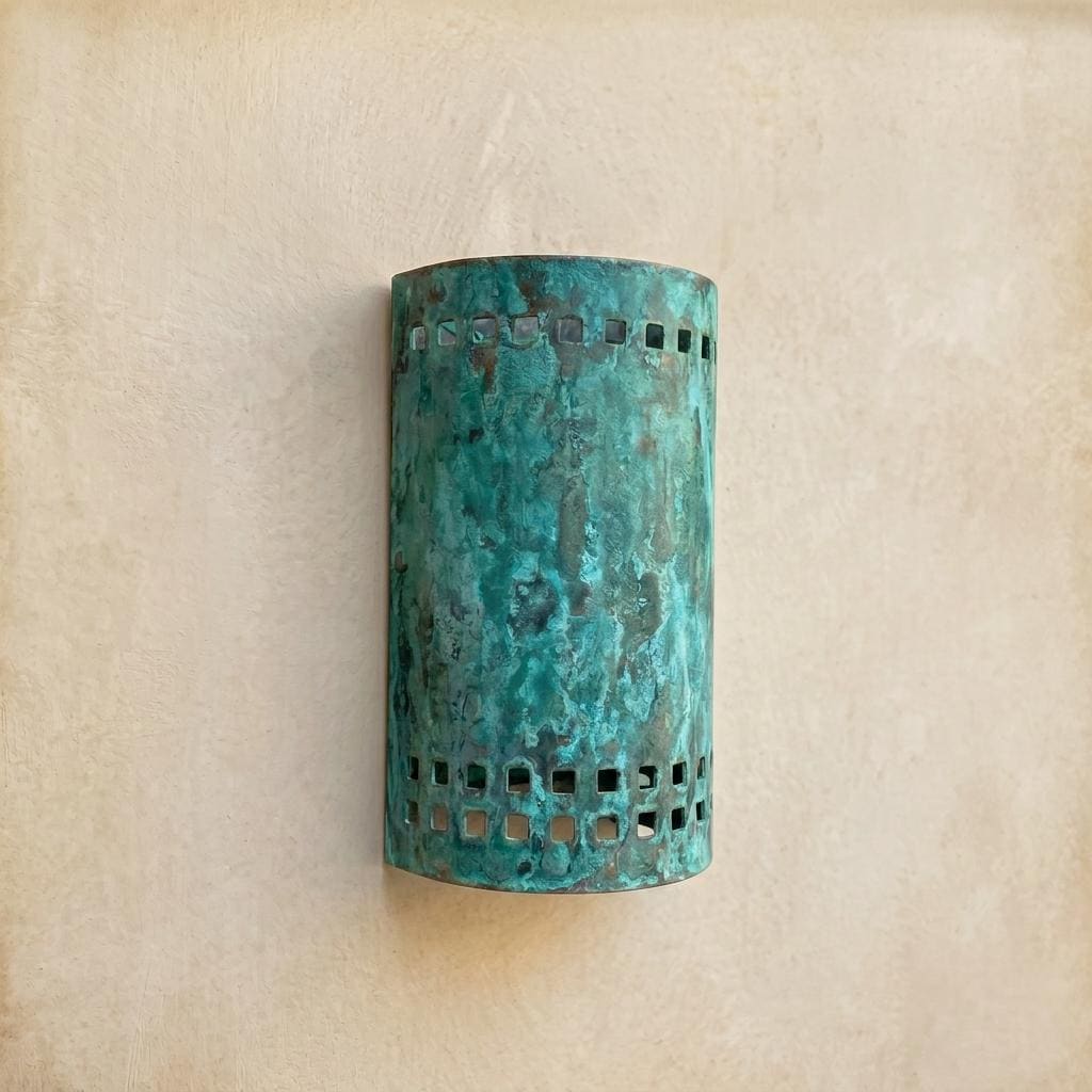 A cylindrical wall sconce with a distressed turquoise and green patina finish, featuring square cutout details near the top and bottom, mounted on a textured beige wall.