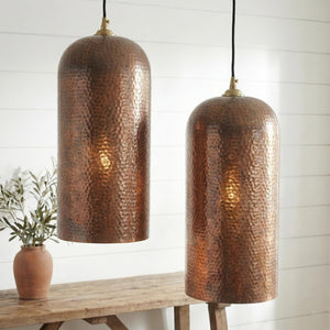 Two copper pendant lights hanging above a wooden table with a plant in the background.