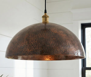 Hammered copper pendant light hanging in a room with white walls and a window.