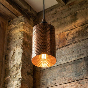 Hammered copper pendant light hanging against a rustic wooden wall.