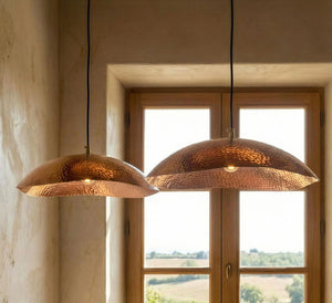 Two copper pendant lights hanging in front of a window with a view of greenery.