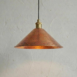 Copper pendant light with brass fitting against a textured white wall
