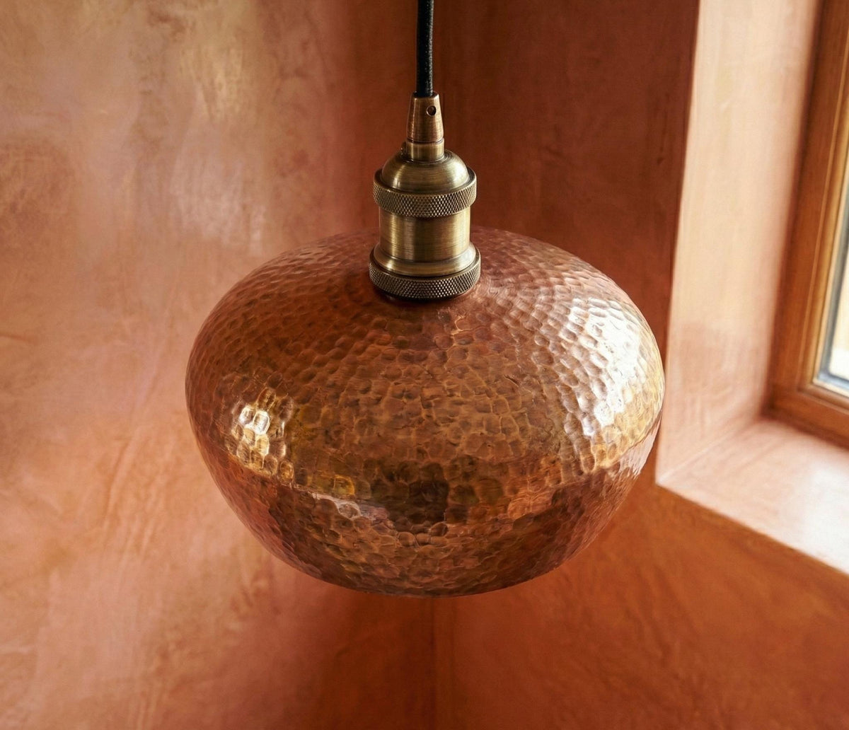 Copper pendant light with textured surface against a warm-toned wall.