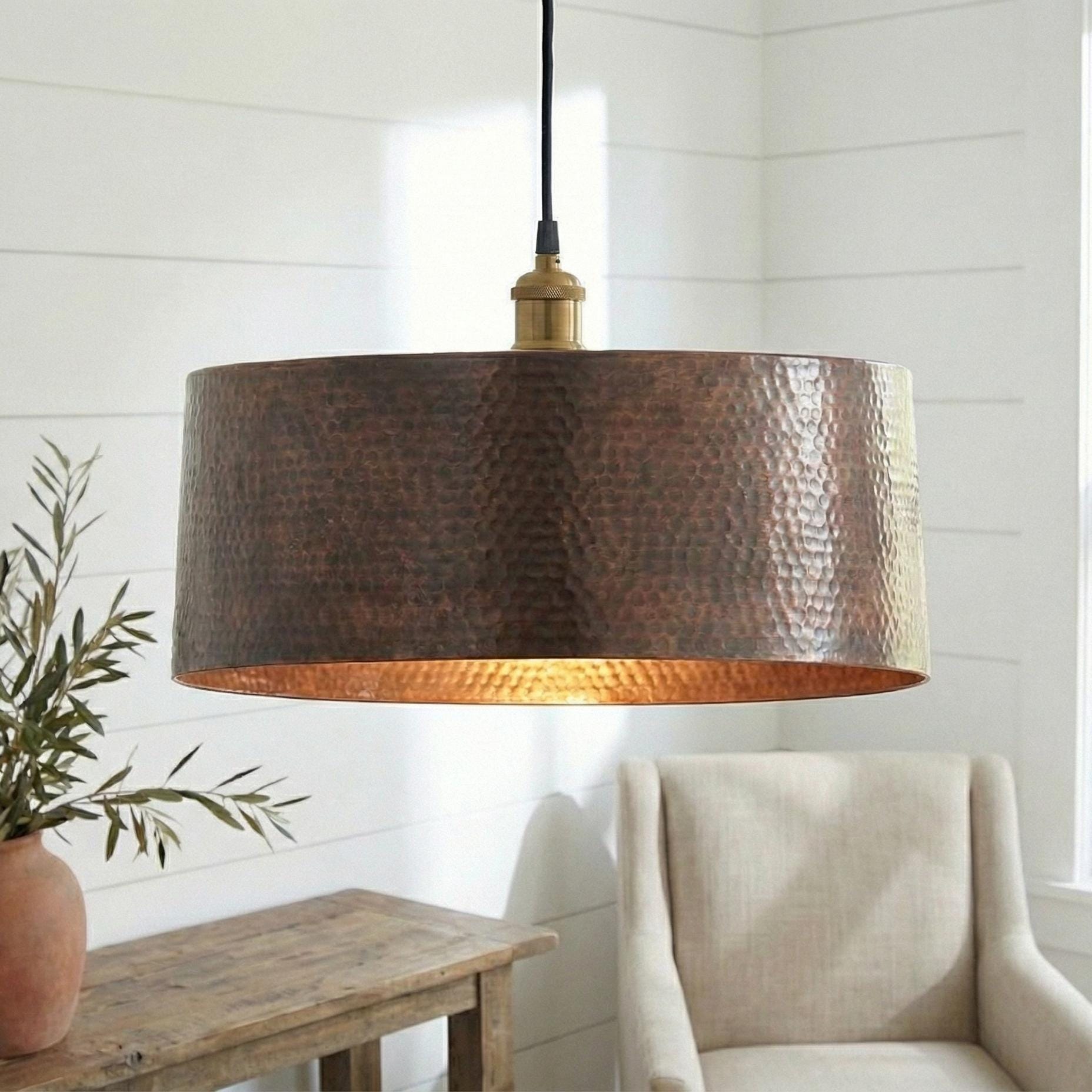 Hammered copper pendant light hanging in a room with a plant and chair.