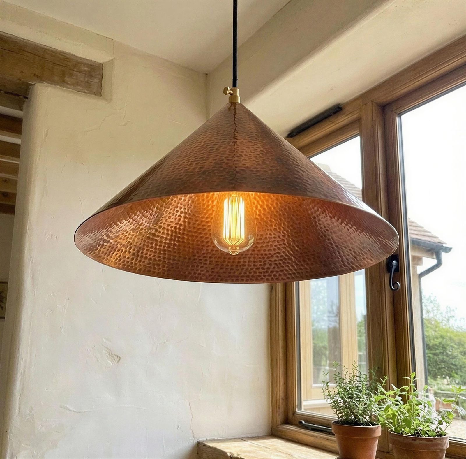Copper pendant light hanging in a room with large windows and plants.