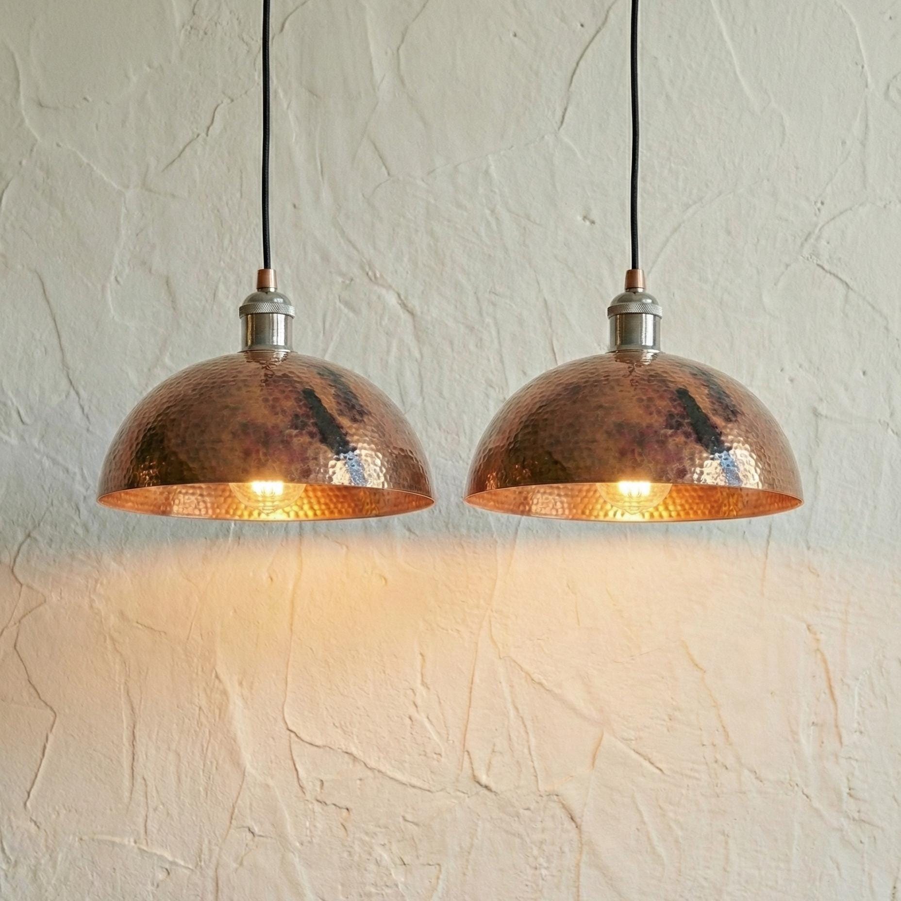 Two copper pendant lights hanging against a textured white wall.