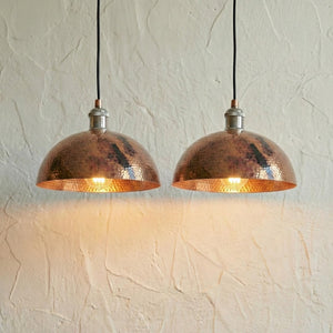 Two copper pendant lights hanging against a textured white wall.