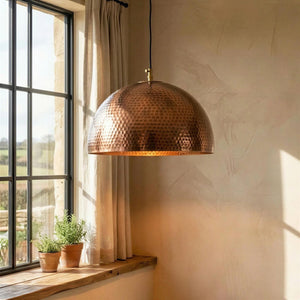 Copper pendant light hanging in a room with a window and plants.
