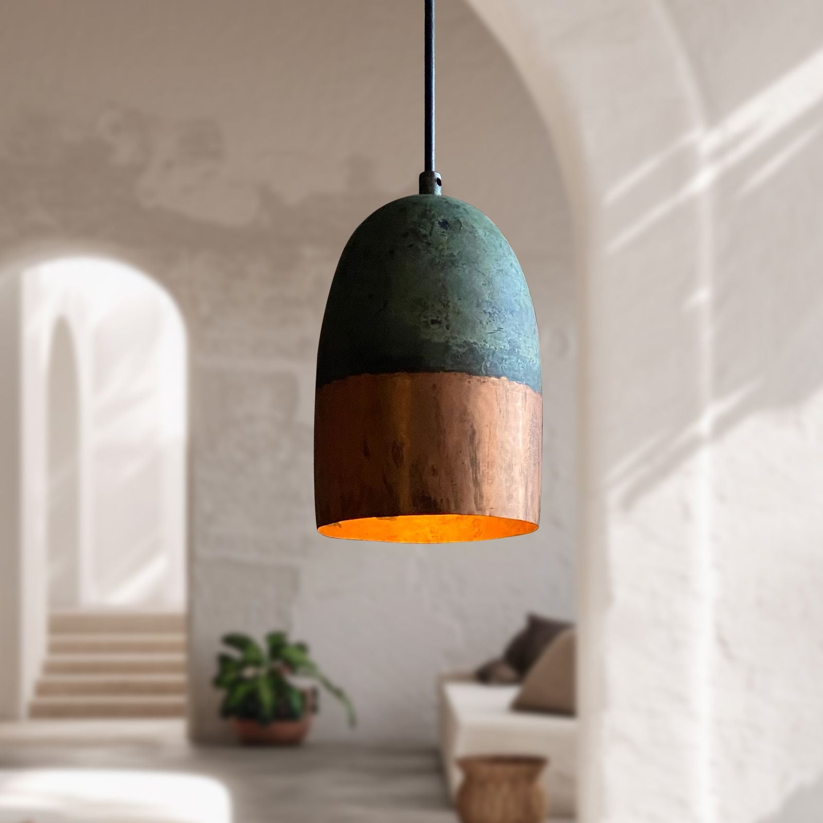 Pendant light with a green and wooden design hanging in a room with a plant and sofa.
