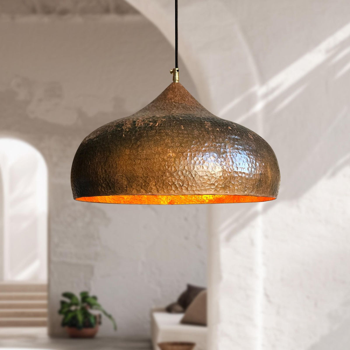 Hammered metal pendant light hanging in a room with a blurred background