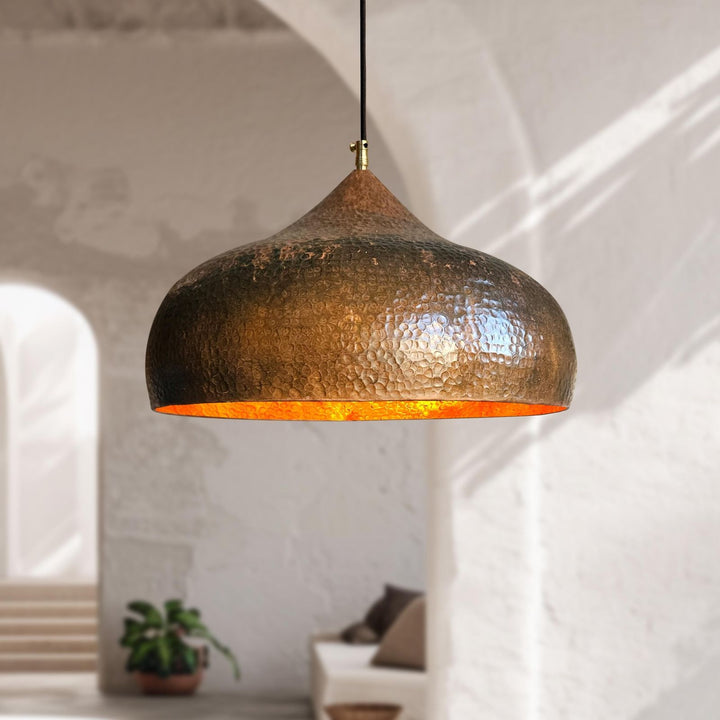 Hammered metal pendant light hanging in a room with a blurred background