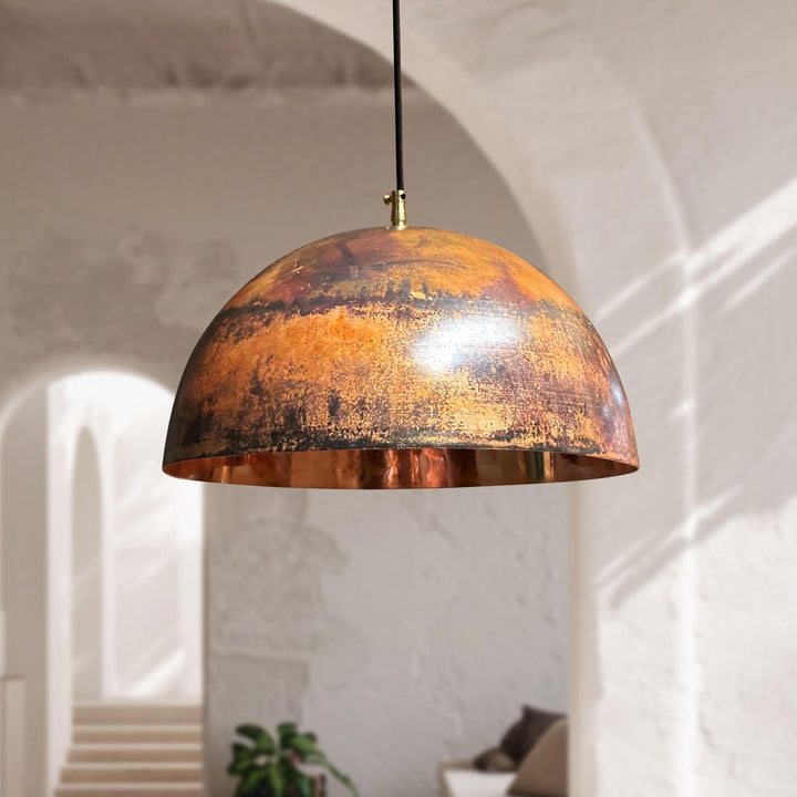 Bronze pendant light hanging in a room with white walls and a plant.