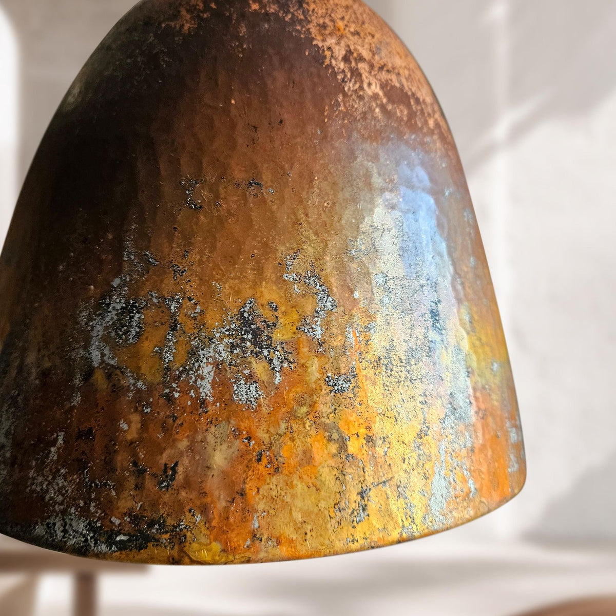 A close-up of a dome-shaped lampshade with a rustic, oxidized finish showing a blend of orange, brown, black, and light blue metallic colors.