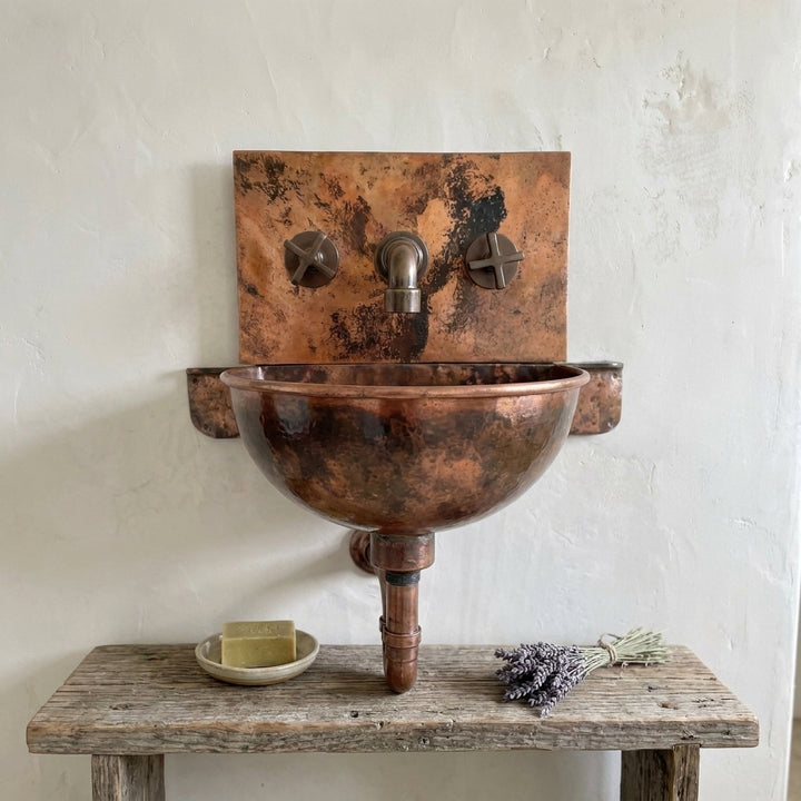 Front view of rustic patina copper wall sink with cross-handle faucet