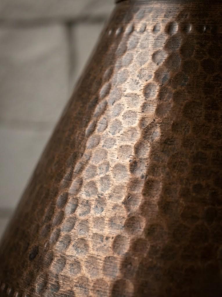 Close-up of a hammered metal surface with a warm copper-brown tone and a softly blurred light gray background.