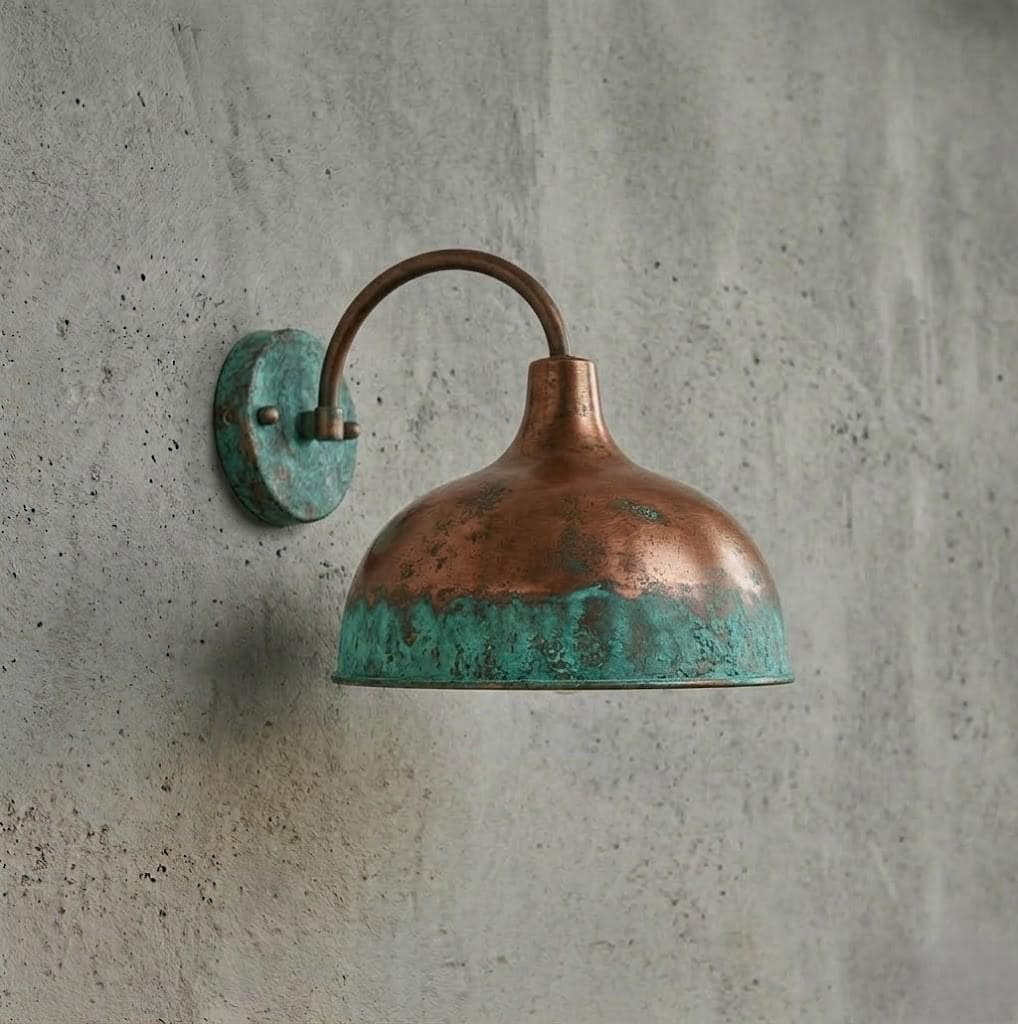 A vintage-style industrial wall sconce with a hammered copper dome shade and a turquoise verdigris patina, mounted on a textured gray concrete wall.