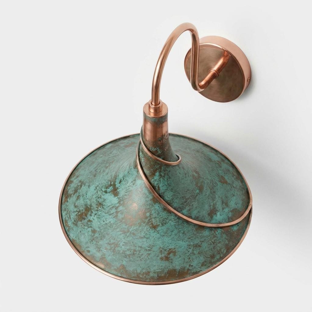 A vintage-style wall sconce with a large dome-shaped shade featuring a distressed green and bronze patina, accented by a curved copper-toned metal arm and circular wall mount on a light gray background.