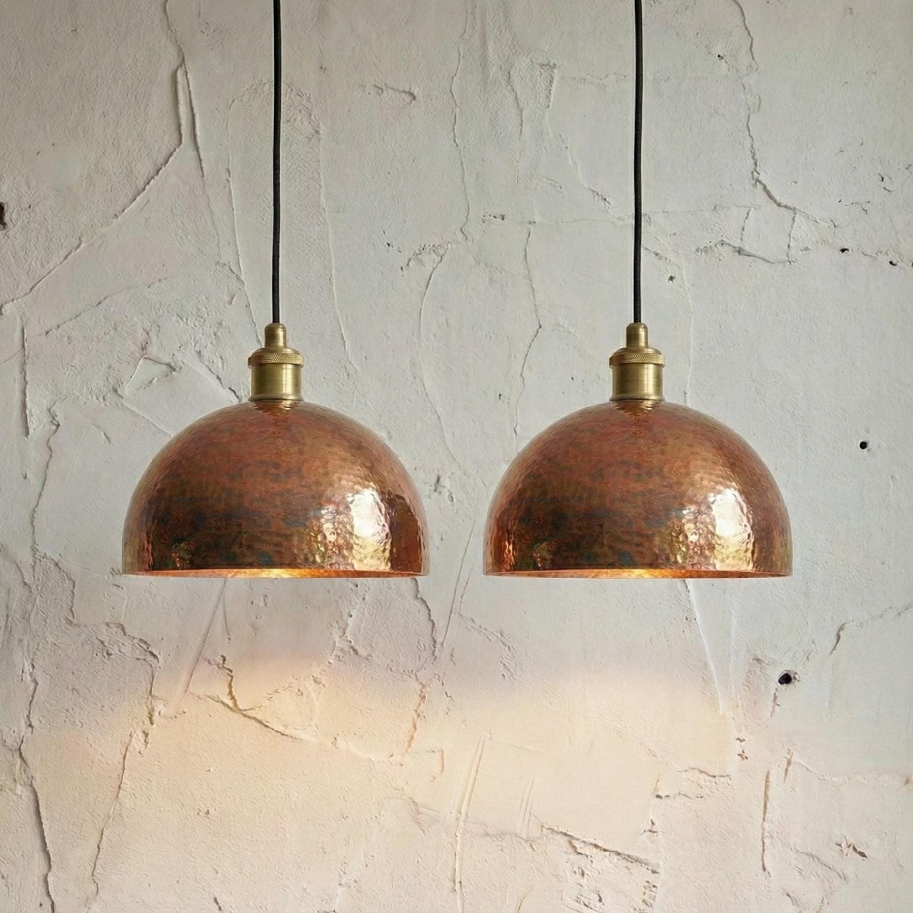 Two copper pendant lights hanging against a textured white wall.