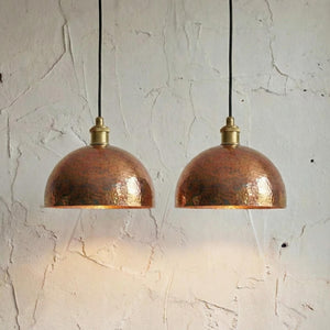 Two copper pendant lights hanging against a textured white wall.