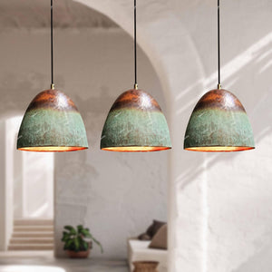 Three pendant lights with green and brown distressed finish hanging in a room with white walls and a plant.