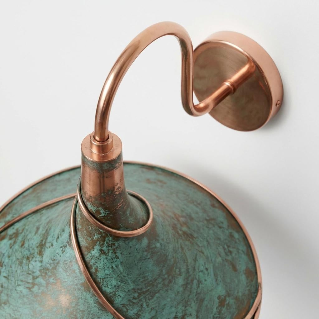 A close-up of a wall-mounted sconce with a distressed copper finish and a green verdigris-textured shade, shown against a plain light background.