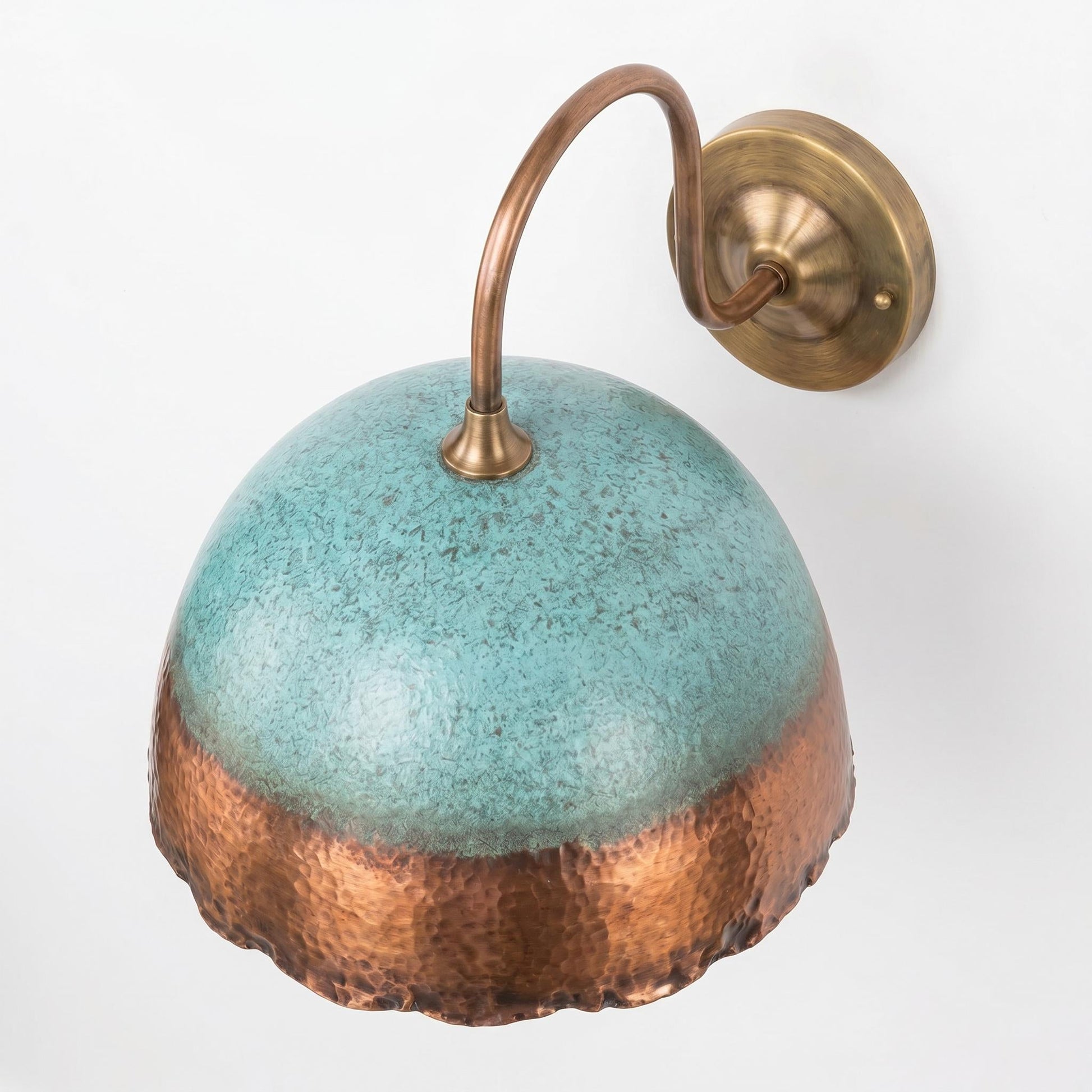 A wall-mounted sconce with a dome-shaped shade featuring a turquoise glaze on the upper half and a hammered copper finish on the lower half, attached to a curved brass arm and round wall plate against a white background.