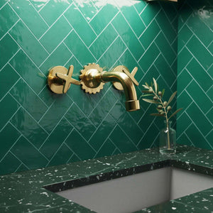 Gold faucet on a green tiled wall with a green countertop.