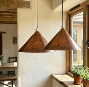 Two copper pendant lights hanging in a room with a window and table.