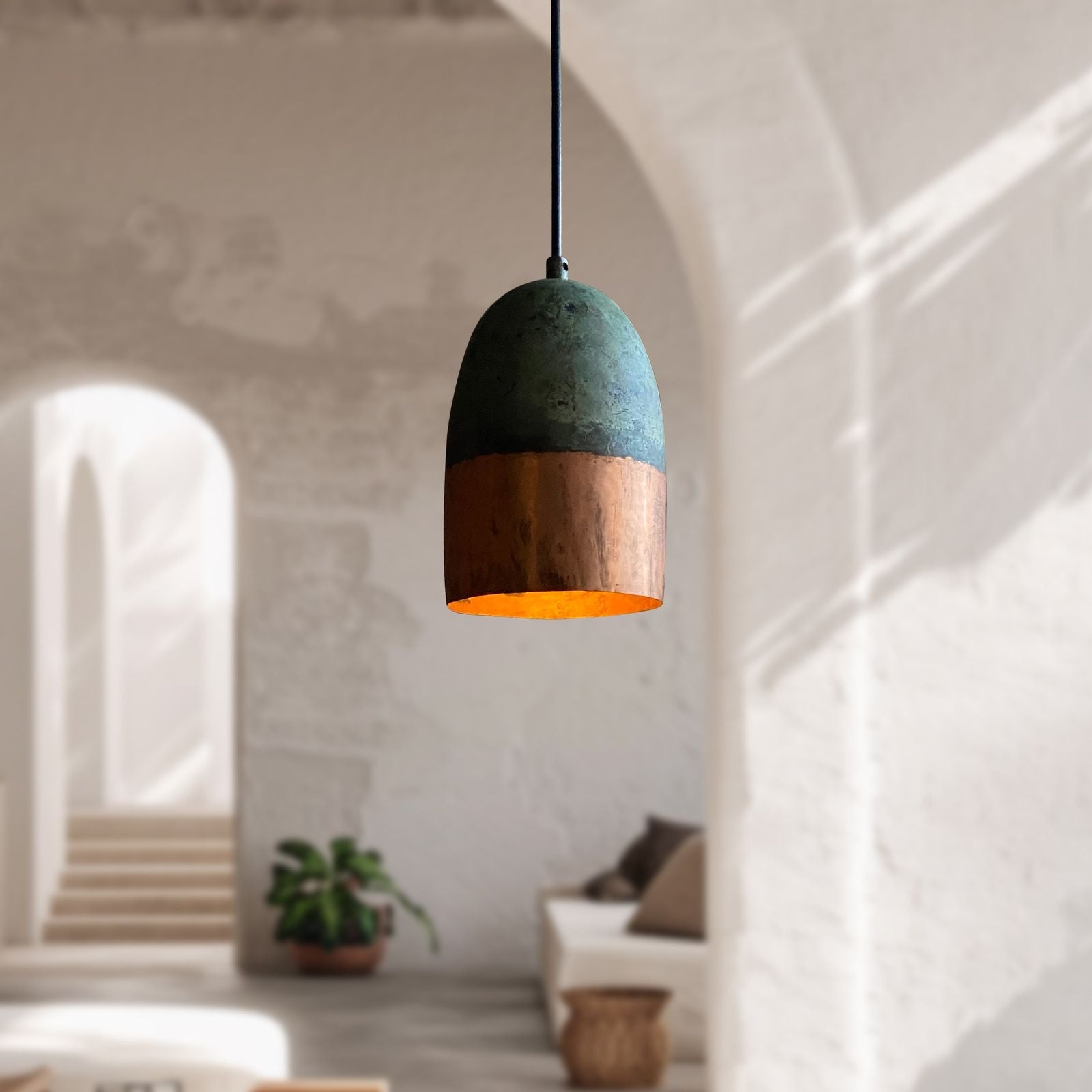 Pendant light with green top and copper bottom in a blurred room setting
