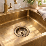 Unlacquered brass kitchen sink drain strainer installed in an aged brass sink