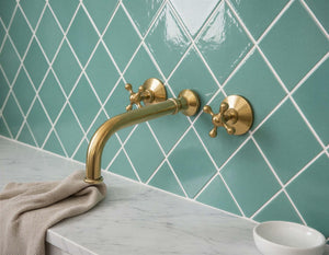 Gold faucet on a tiled wall with a towel and soap dish in the foreground