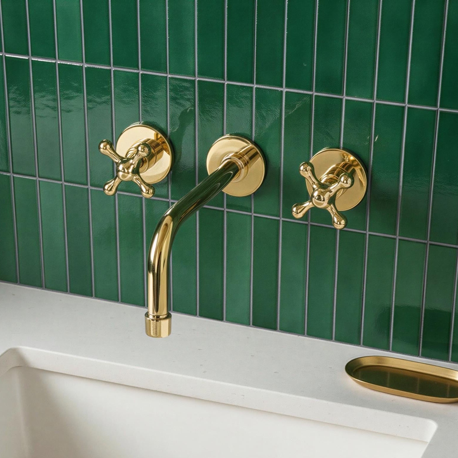 Gold faucet and handles on a green tiled wall with a white sink.
