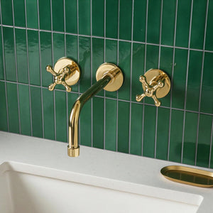 Gold faucet and handles on a green tiled wall with a white sink.