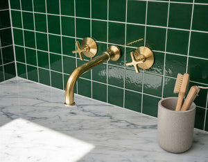 Gold faucet on a marble countertop with green tiled wall