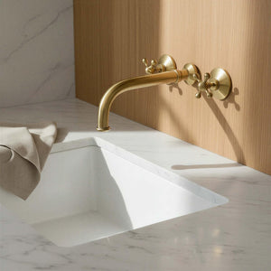 Gold faucet on a white sink with marble wall and countertop