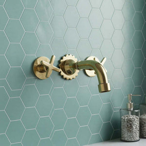 Bathroom sink with gold faucet against a green tiled wall