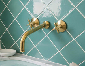 Gold faucet and handles on a teal tiled wall