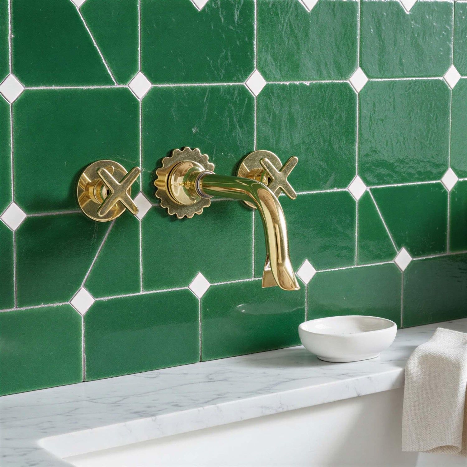 Gold faucet on a green tiled wall with a marble countertop