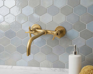 Gold faucet on a hexagonal tiled wall with a white soap dispenser.