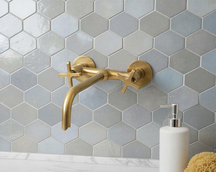 Gold faucet on a hexagonal tiled wall with a white soap dispenser.